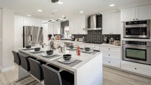 Una cocina moderna con armarios blancos, una isla central y electrodomésticos integrados, como refrigerador, horno y microondas.