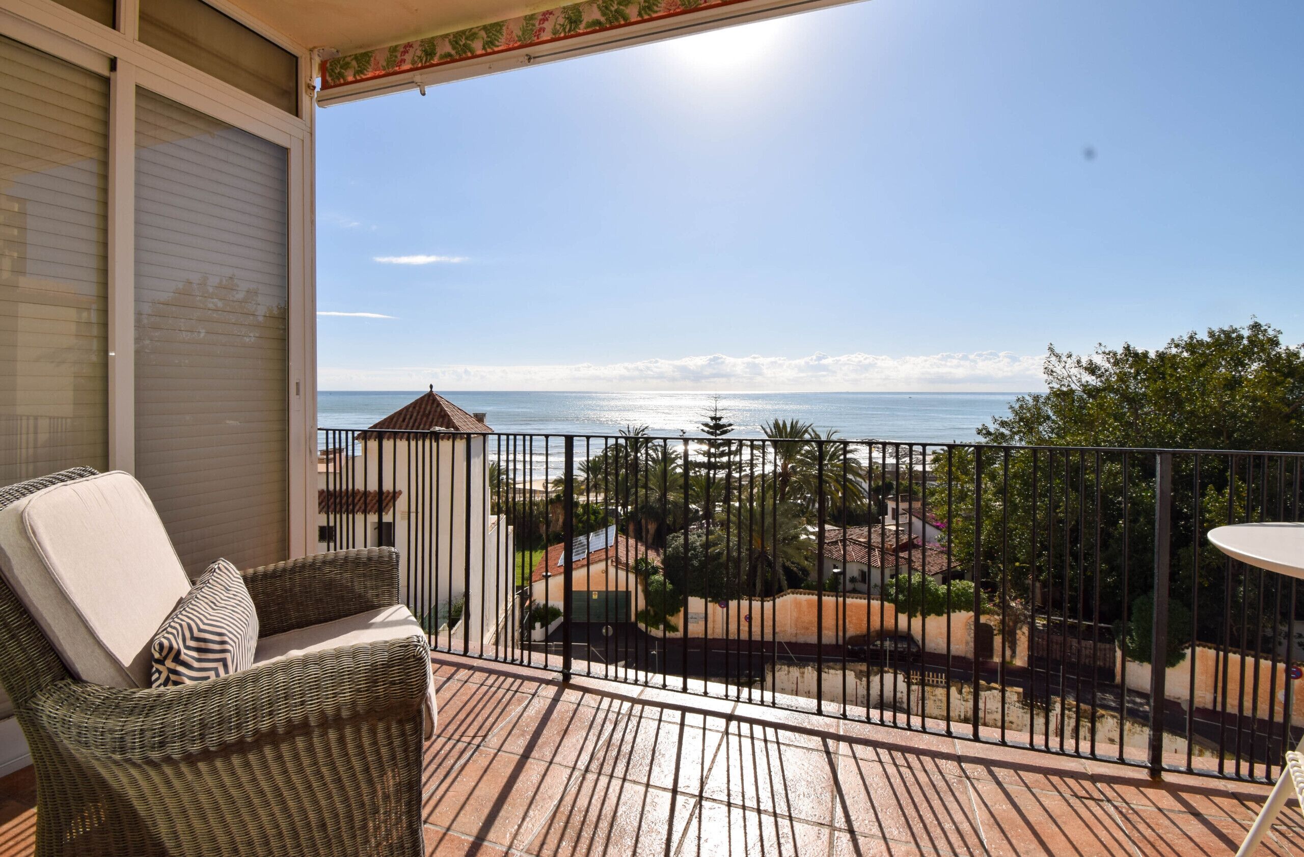 Un balcon doté de meubles en osier, offrant une vue sur la mer et muni d’une balustrade.