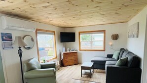 A living room with a wooden ceiling, a sofa, a chair, a coffee table, a TV, and a window.