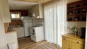 Una cocina compacta con electrodomésticos blancos, armarios de madera y una ventana con cortinas translúcidas.