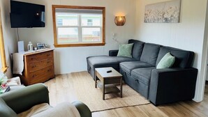 A living room with a sofa, a television, a wooden dresser, and a window.