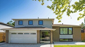 Una moderna casa a due piani con garage, un'ampia finestra al secondo piano e un prato curato.