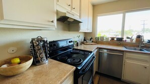 Una cocina con estufa, horno y lavabo. Hay una ventana que proporciona luz natural y vistas al exterior.