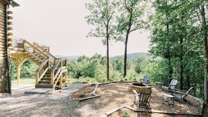 Una scala in legno conduce a una baita, con un'area relax e un focolare circondati da sedie, e una vista su un paesaggio boschivo.