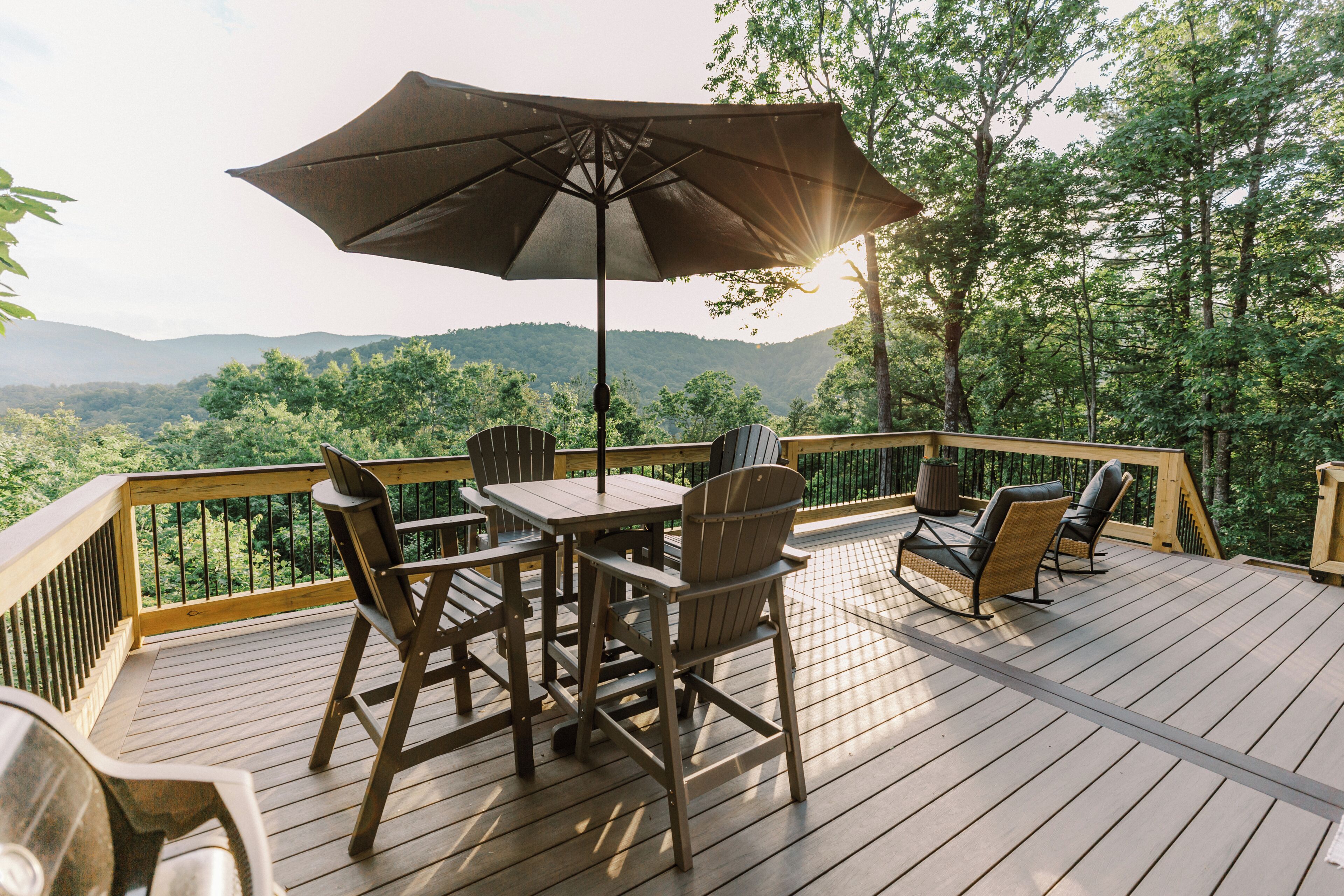 A wooden deck with outdoor furniture, including chairs and a table, overlooking a forested area.