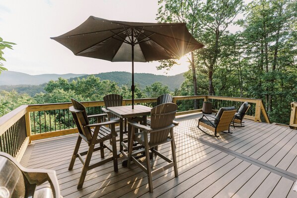 A wooden deck with outdoor furniture, including chairs and a table, overlooking a forested area.