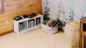 A room with wooden walls, a sloped ceiling, a bookshelf, a basket, and wall decorations.