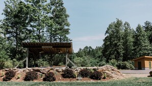 A wooden pavilion with a sign, surrounded by landscaped garden beds and trees.