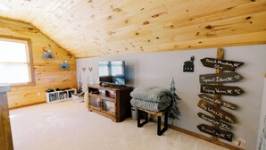 A cozy room with a wooden ceiling, a television, a bookshelf, and a wall with directional signs.