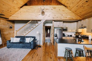 A wooden interior with a sofa, kitchen, and staircase.