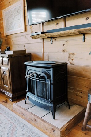 A room with a black wood-burning stove, a television mounted on the wall, and a wooden cabinet. - Cozy 2BR with AMAZING views in Buck Mountain (Purlear)