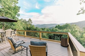 A deck with outdoor furniture, a railing, and a view of a forested mountain range.