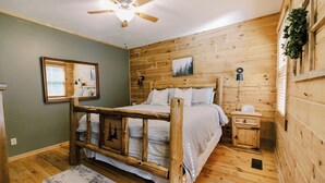 A wooden bedroom with a bed, a nightstand, a mirror, and a ceiling fan.