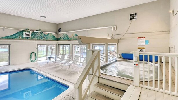 An indoor swimming pool with a clear view of the pool area, a set of stairs leading to a changing room, and a mural on the wall.