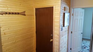 A wooden-paneled hallway with a brown door, a coat rack, and a white door in the background.