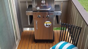 A barbecue grill with a control panel, a round table with a blue mosaic top, and a striped pillow on a wooden deck.