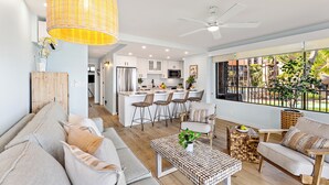 Un salon moderne avec un canapé, une table basse et un coin repas comprenant des chaises, et une cuisine en arrière-plan.
