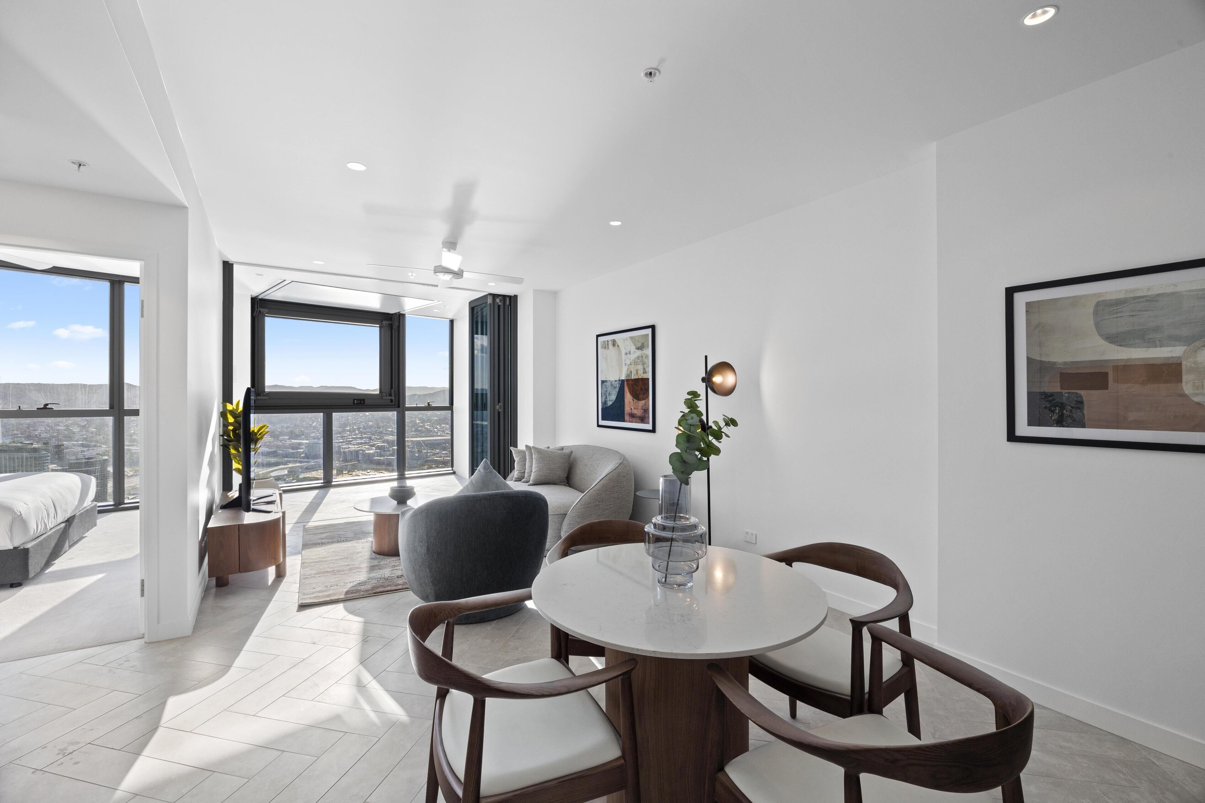 A modern living room with a dining area, large windows, and a city view.