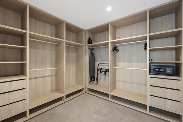 A walk-in closet with multiple wooden shelves and drawers, a hanging rack, and a microwave. - Avani Living Queen’s Wharf Residences (Brisbane)