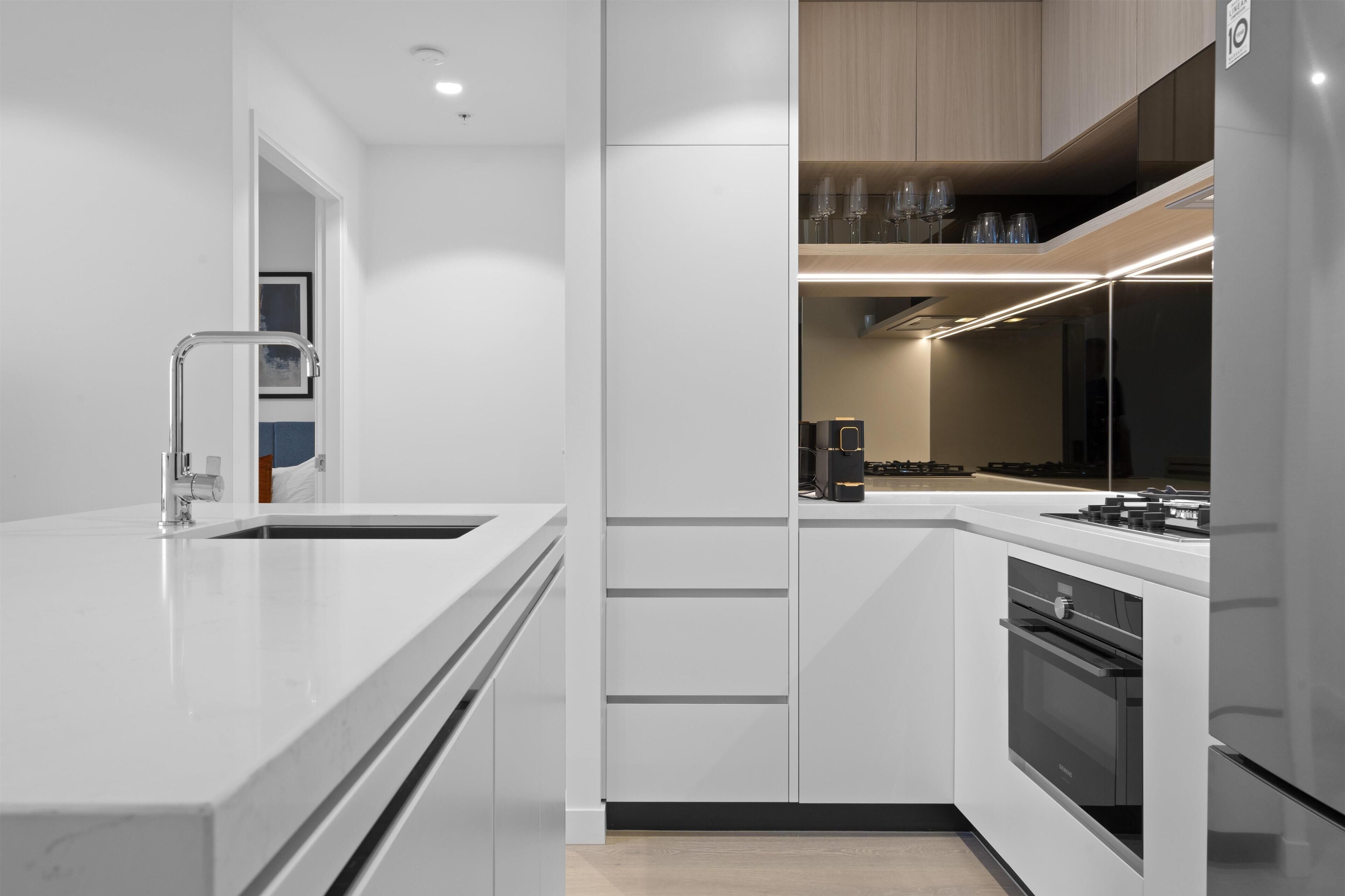 A modern kitchen with white cabinetry, a stainless steel refrigerator, and a built-in oven.
