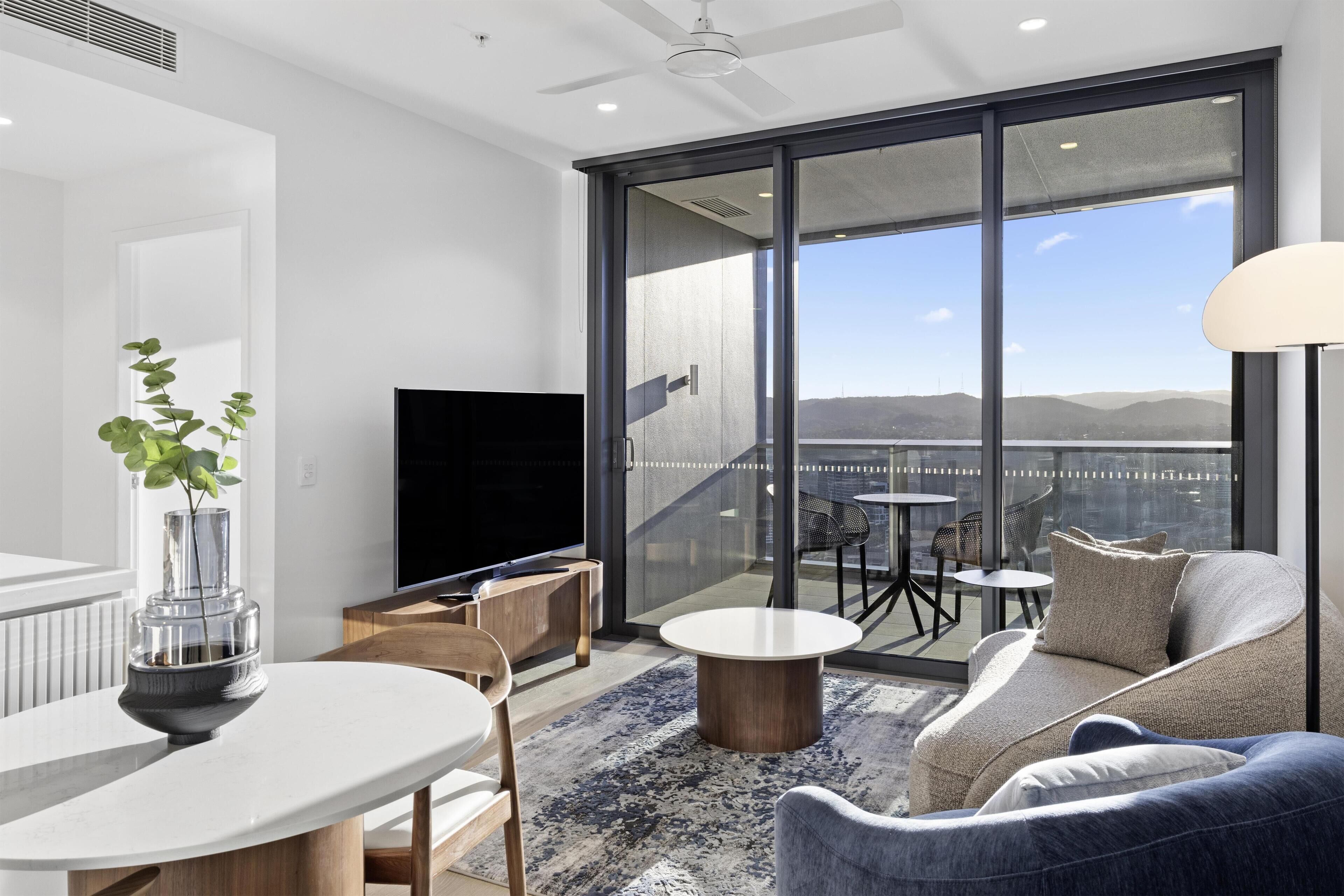 Una sala de estar moderna con un televisor grande, un comedor con mesa y sillas, y un sofá con vistas al exterior.