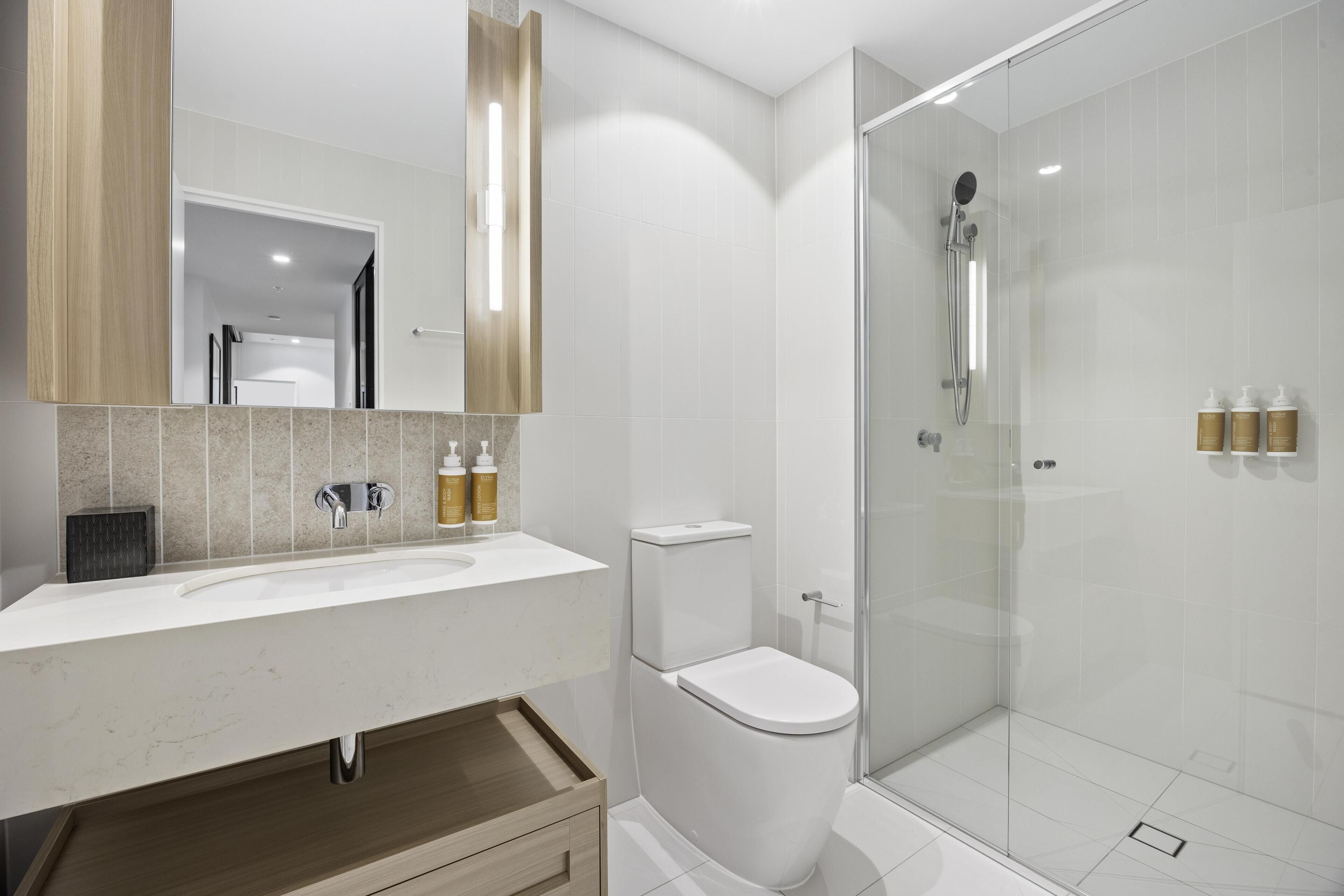 Un baño moderno con un lavamanos blanco, un inodoro y una ducha con mampara de vidrio.