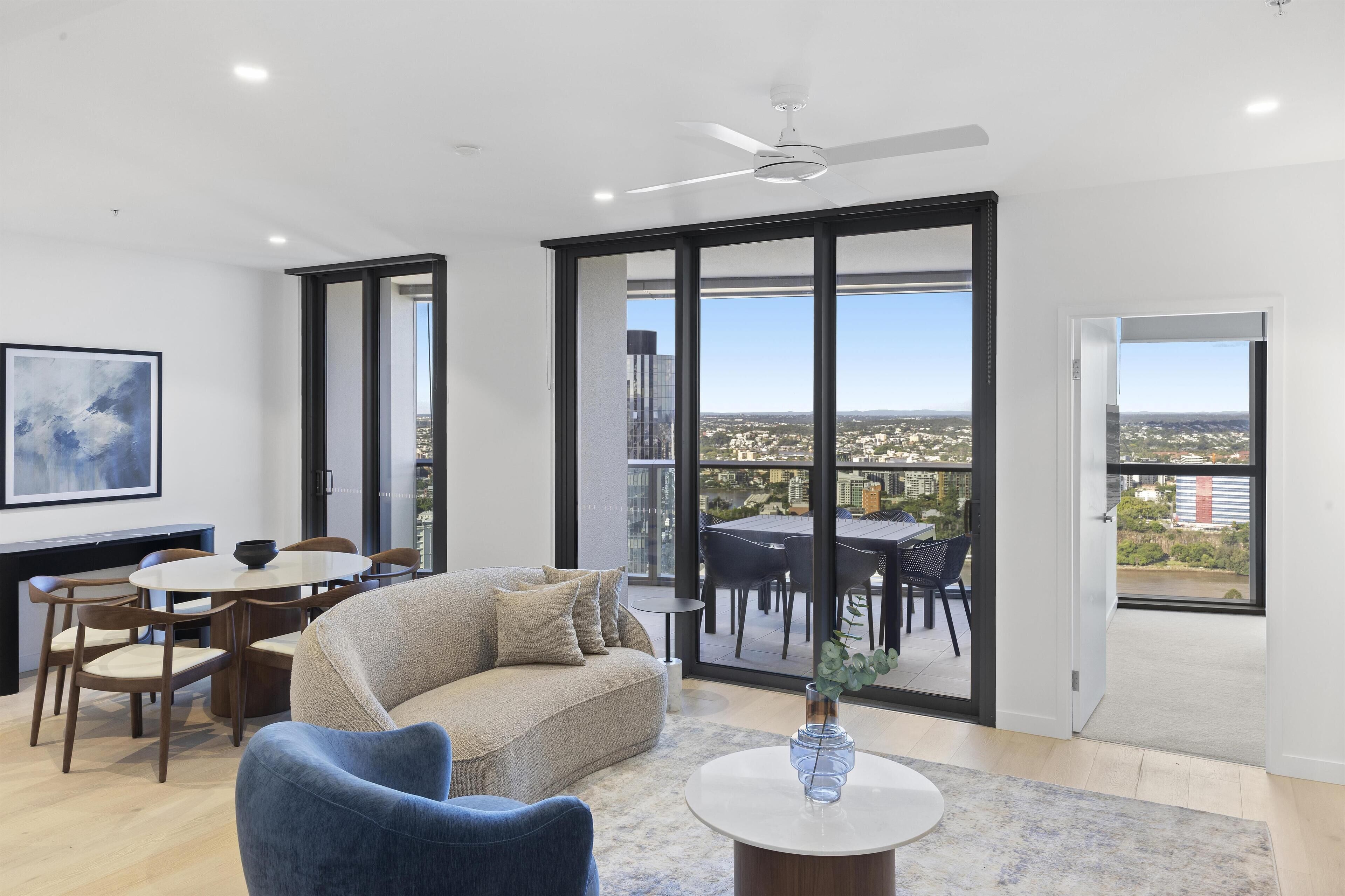 A modern living room with a sofa, chairs, a dining table, and a large window offering a city view.