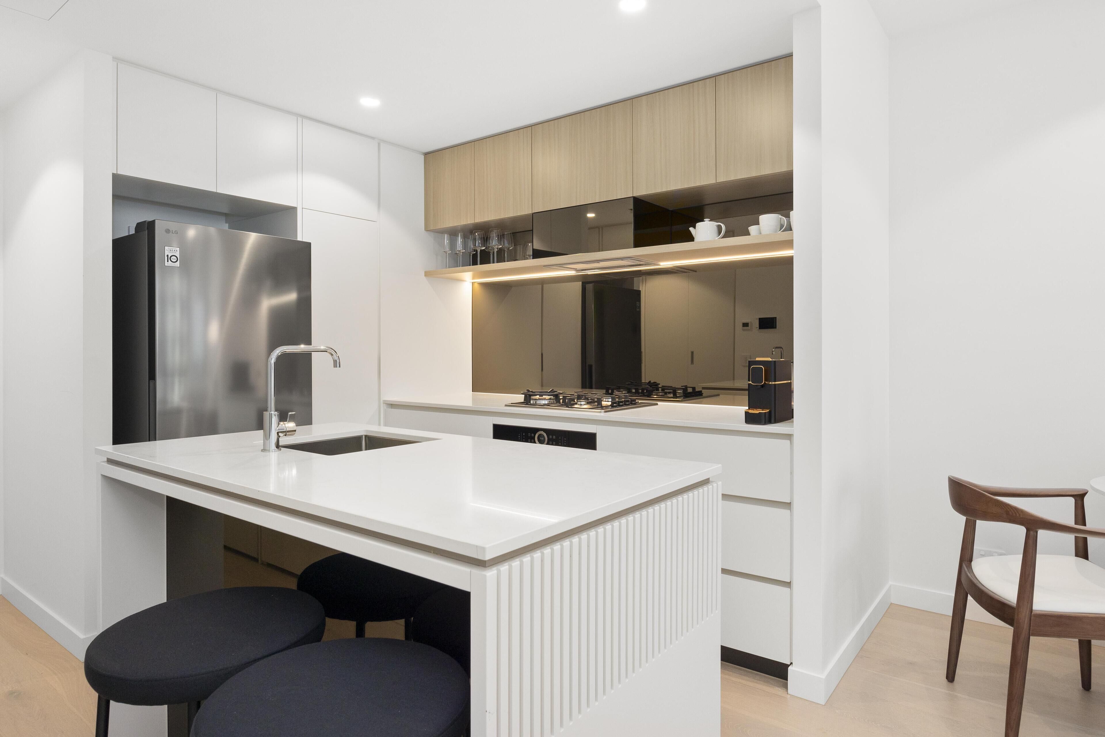 A modern kitchen with white cabinetry, a stainless steel refrigerator, a built-in dishwasher, and a wooden dining area.