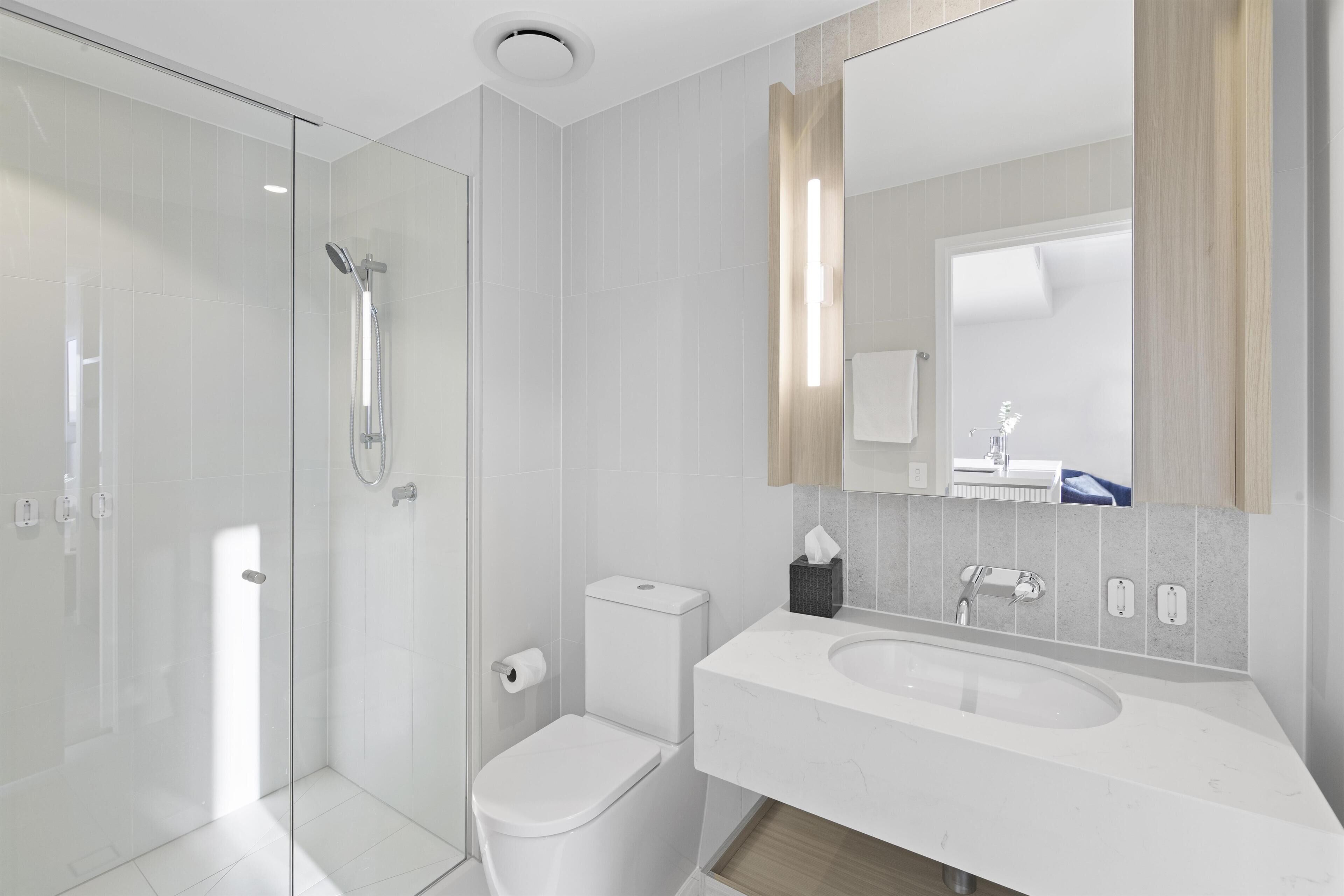 A modern bathroom with a glass shower enclosure, a toilet, and a sink with a mirror above.