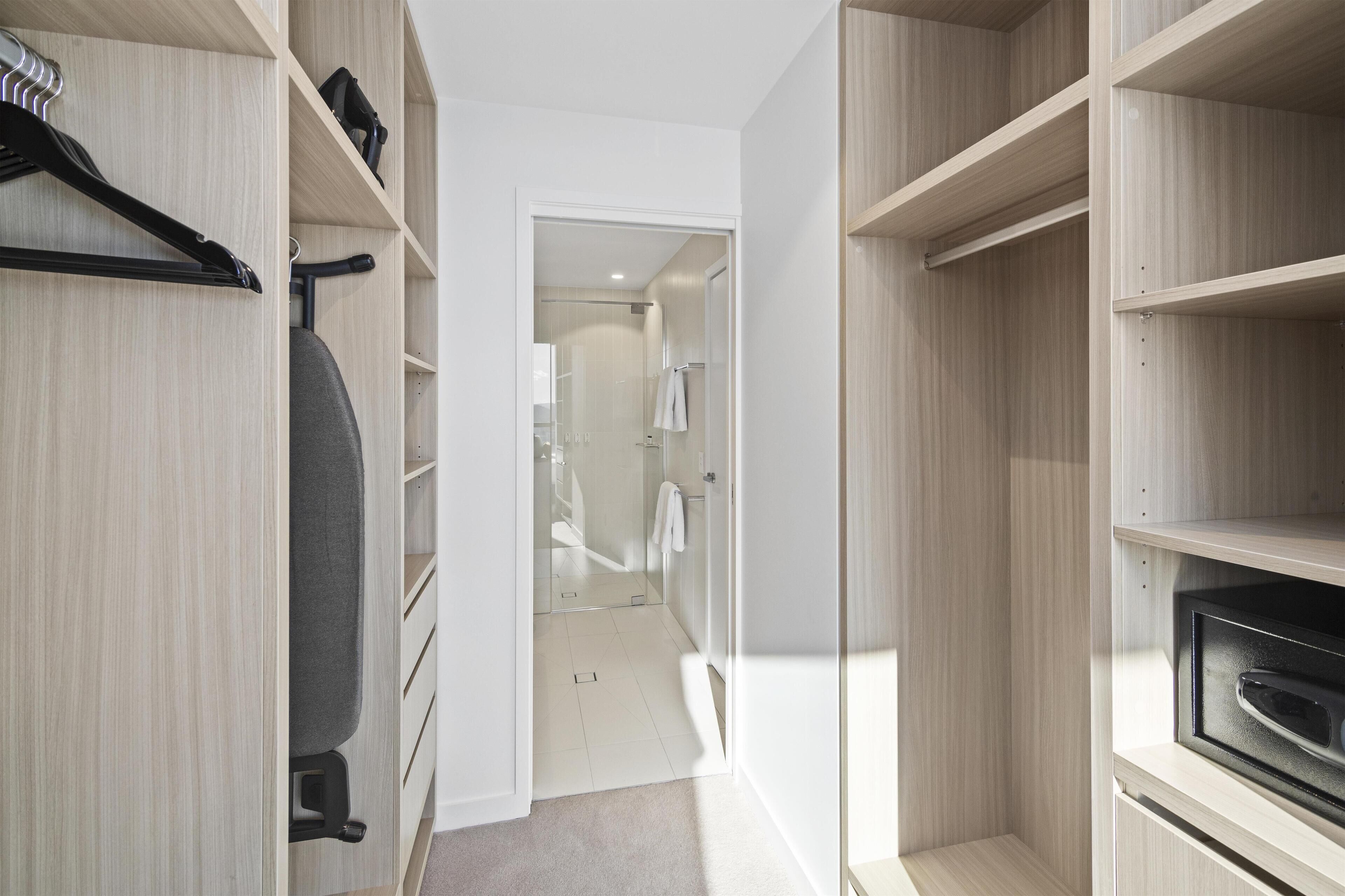 A modern walk-in closet with wooden shelving, a gray chair, and a built-in oven.
