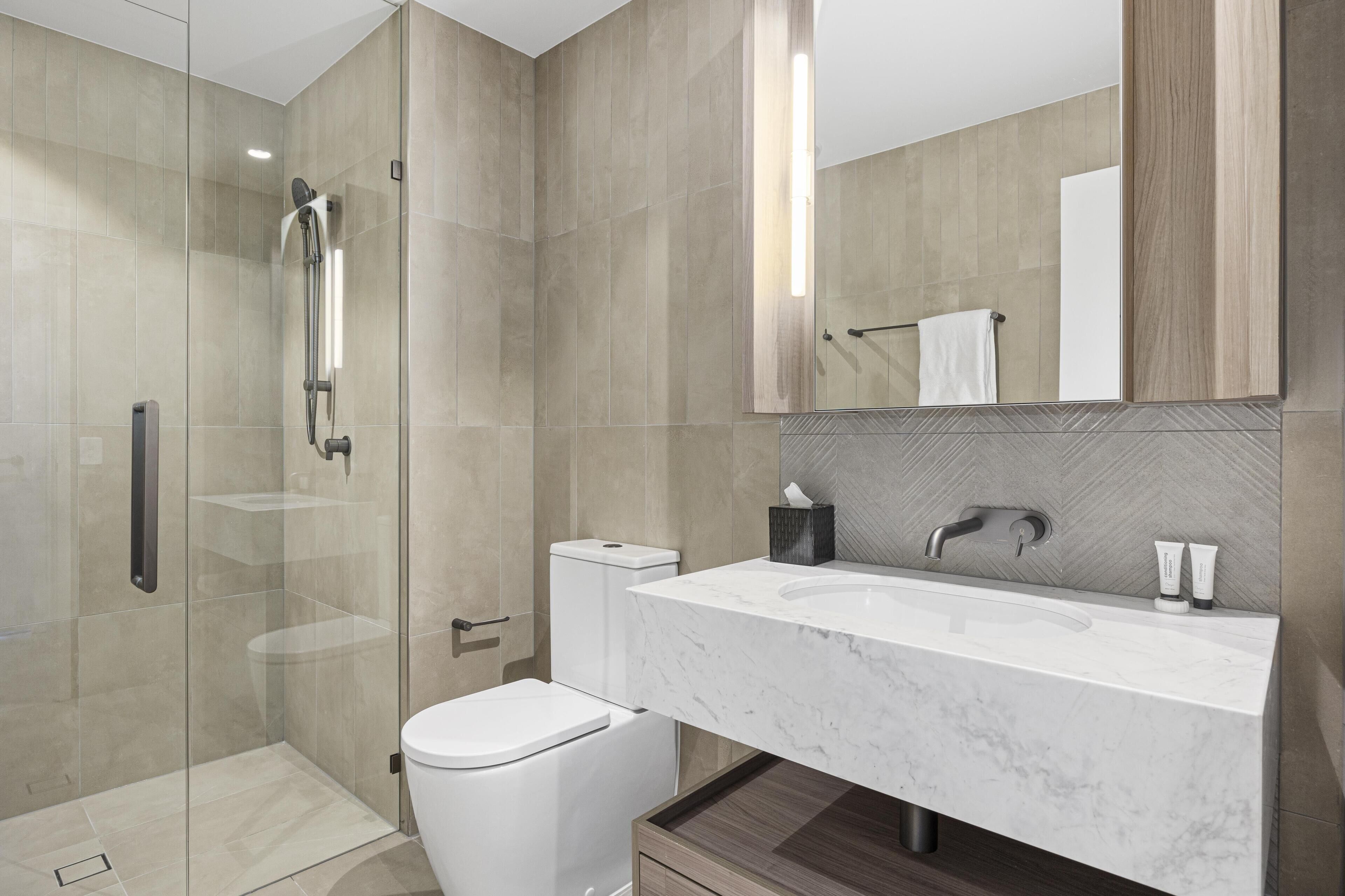 A modern bathroom with a glass-enclosed shower, a white toilet, a marble sink, and a large mirror.