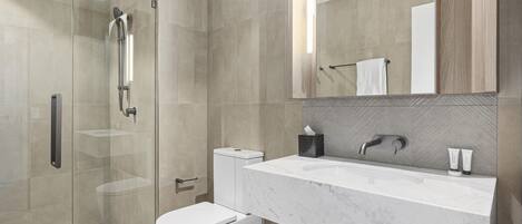 Un baño moderno con ducha de vidrio, inodoro blanco, lavamanos de mármol y un espejo grande.
