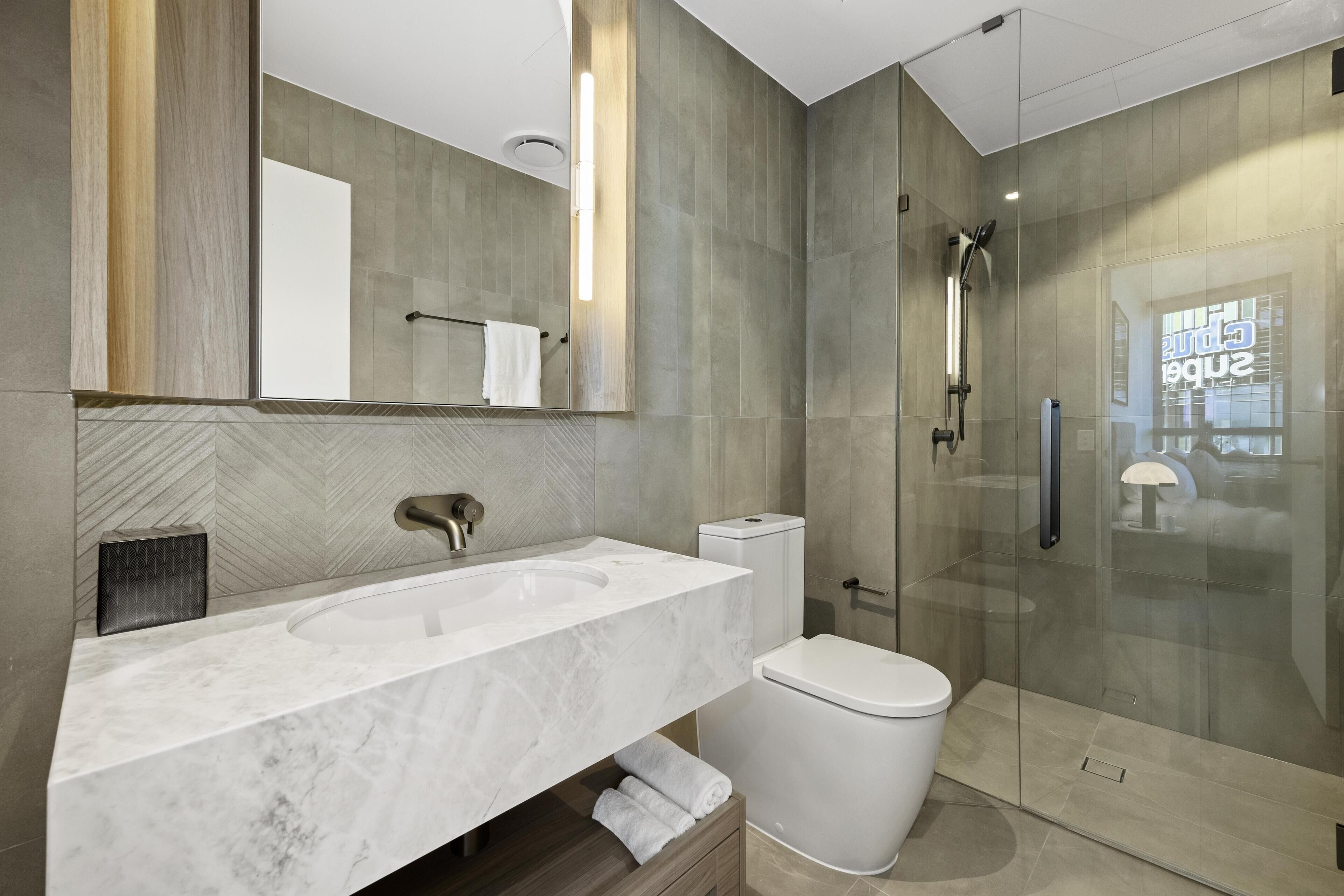 Une salle de bain moderne avec un grand miroir, un lavabo blanc et une douche à parois de verre.