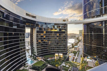 A modern hotel with a curved glass facade, a rooftop pool, and a view of the cityscape.