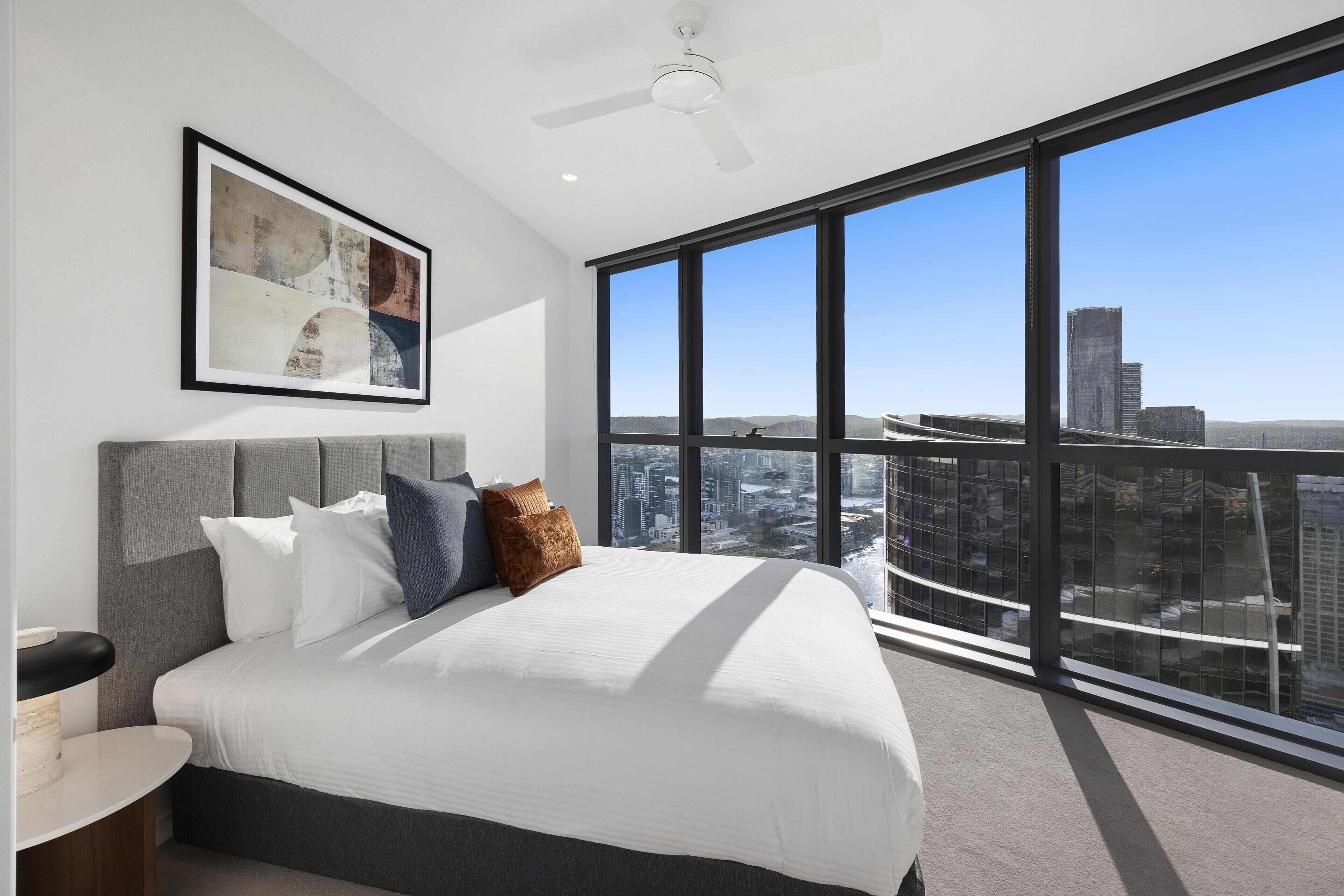 Un dormitorio moderno con una cama grande, vistas a la ciudad y un ventilador de techo.