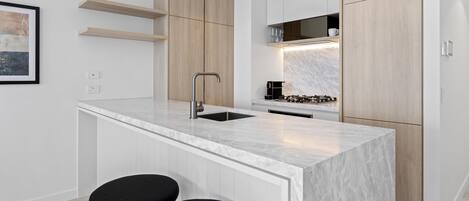A modern kitchen with white cabinetry, a marble countertop, and two black bar stools.
