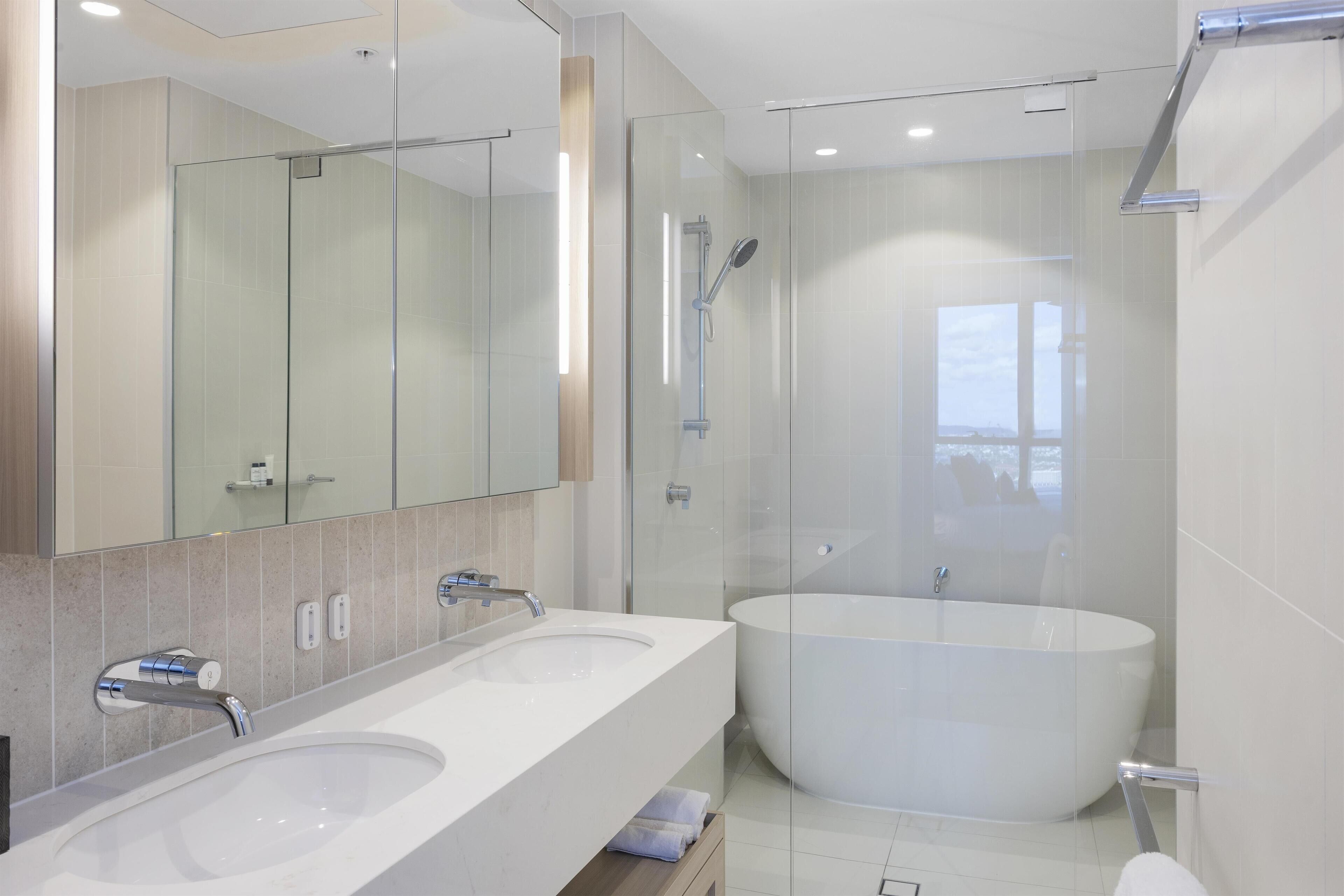Une salle de bain moderne avec deux lavabos, une grande baignoire et une douche séparée par une paroi en verre.