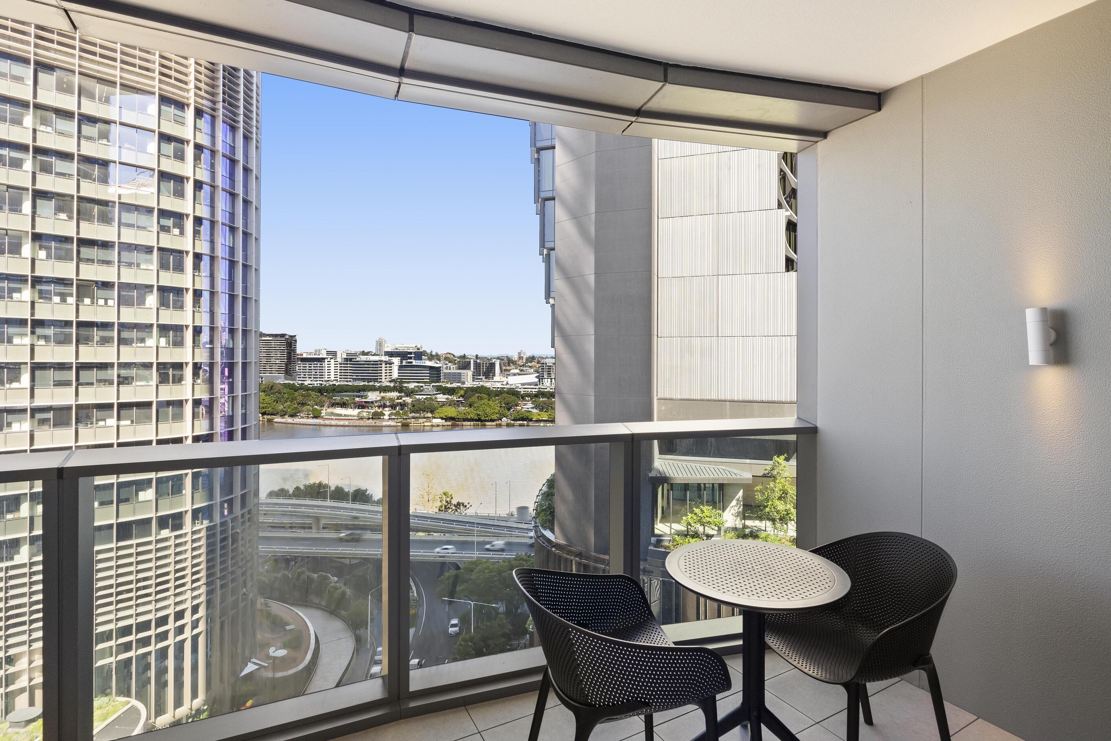 A balcony with a view of a cityscape, two chairs, and a small table.