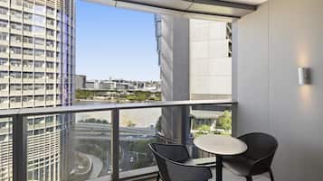 A balcony with a view of a cityscape, two chairs, and a small table.