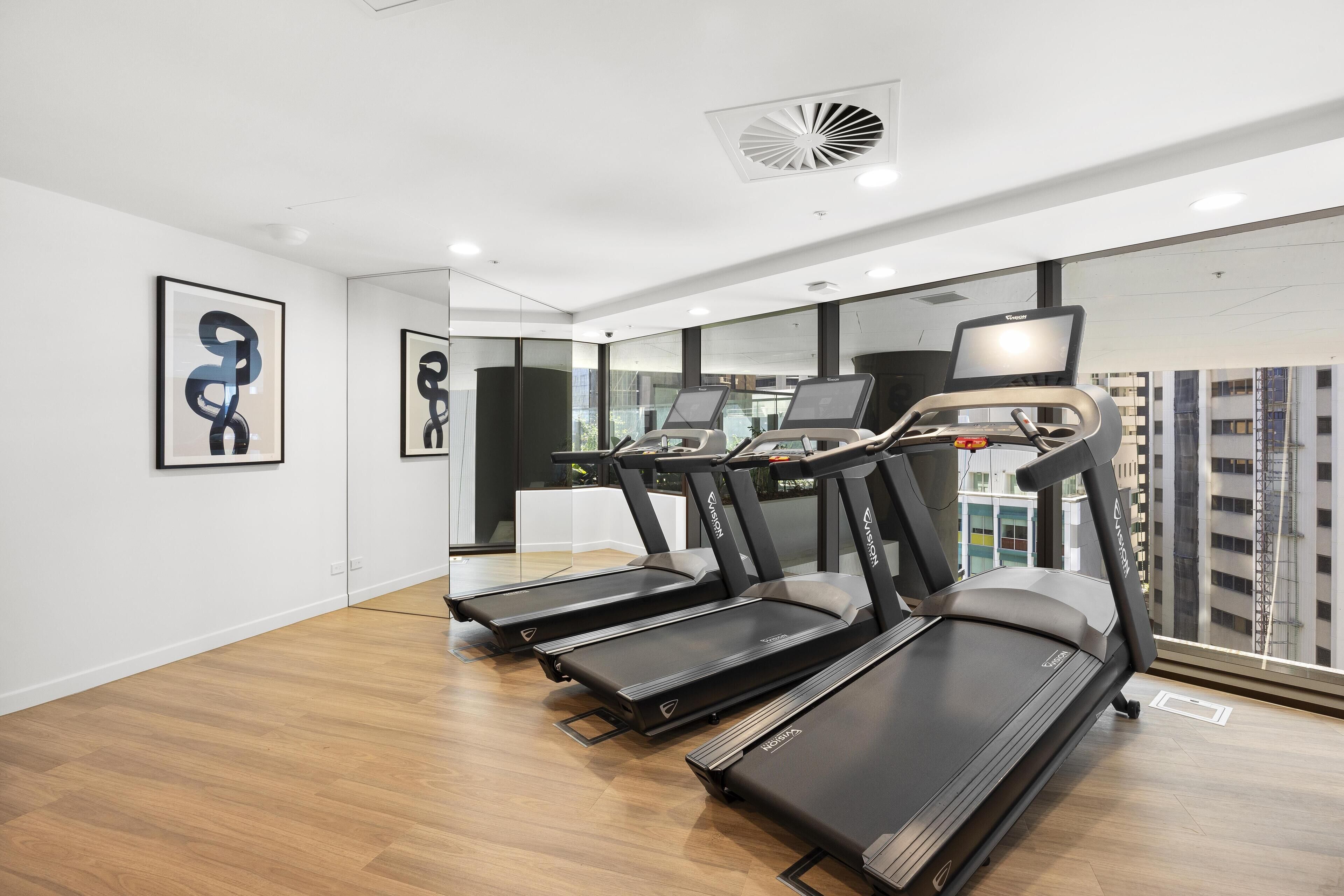 Ein Fitnessraum mit Laufbändern, einem großen Spiegel und Kunstwerken an den Wänden.