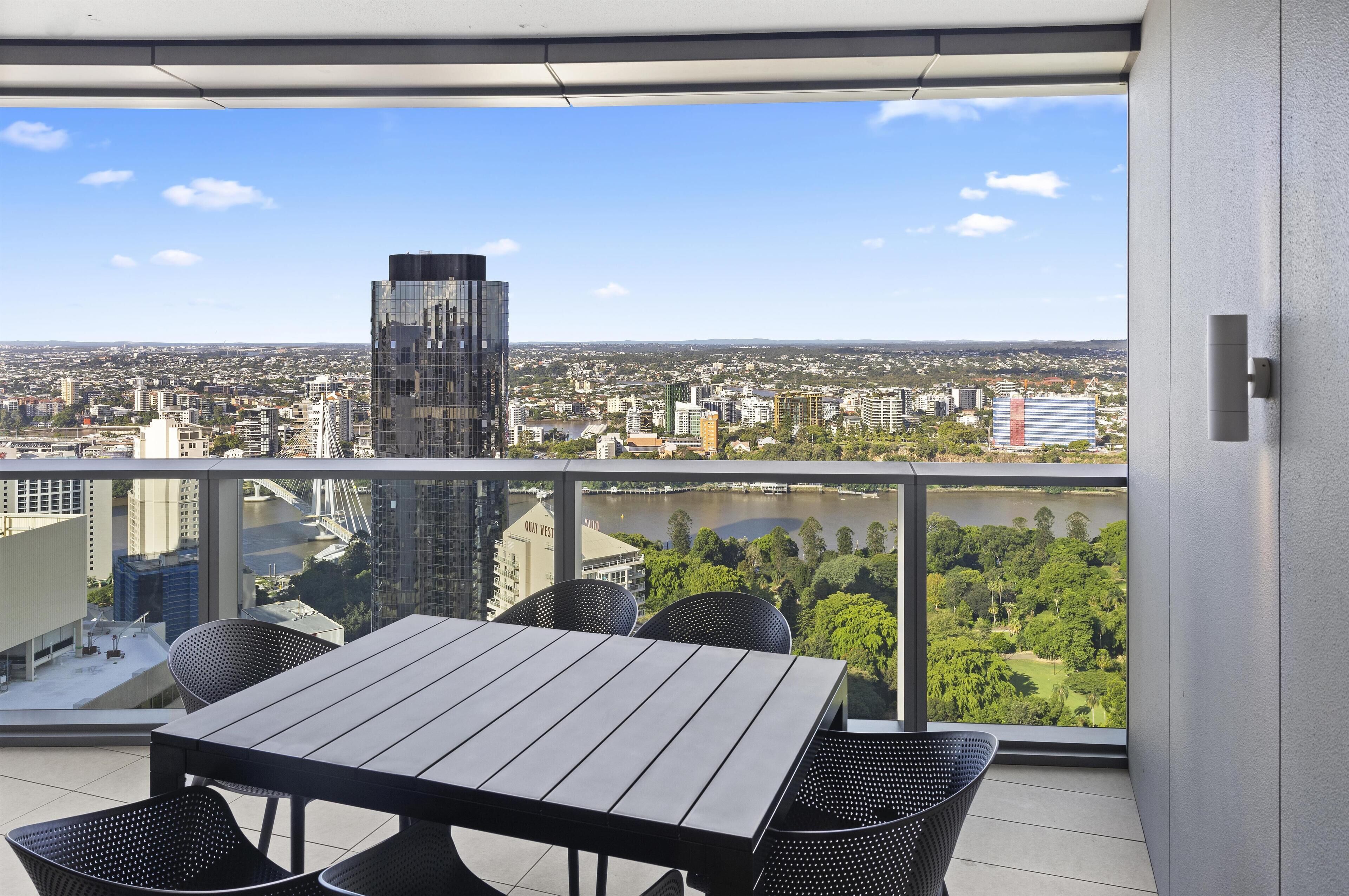 A balcony with a table and chairs, overlooking a cityscape and a river.