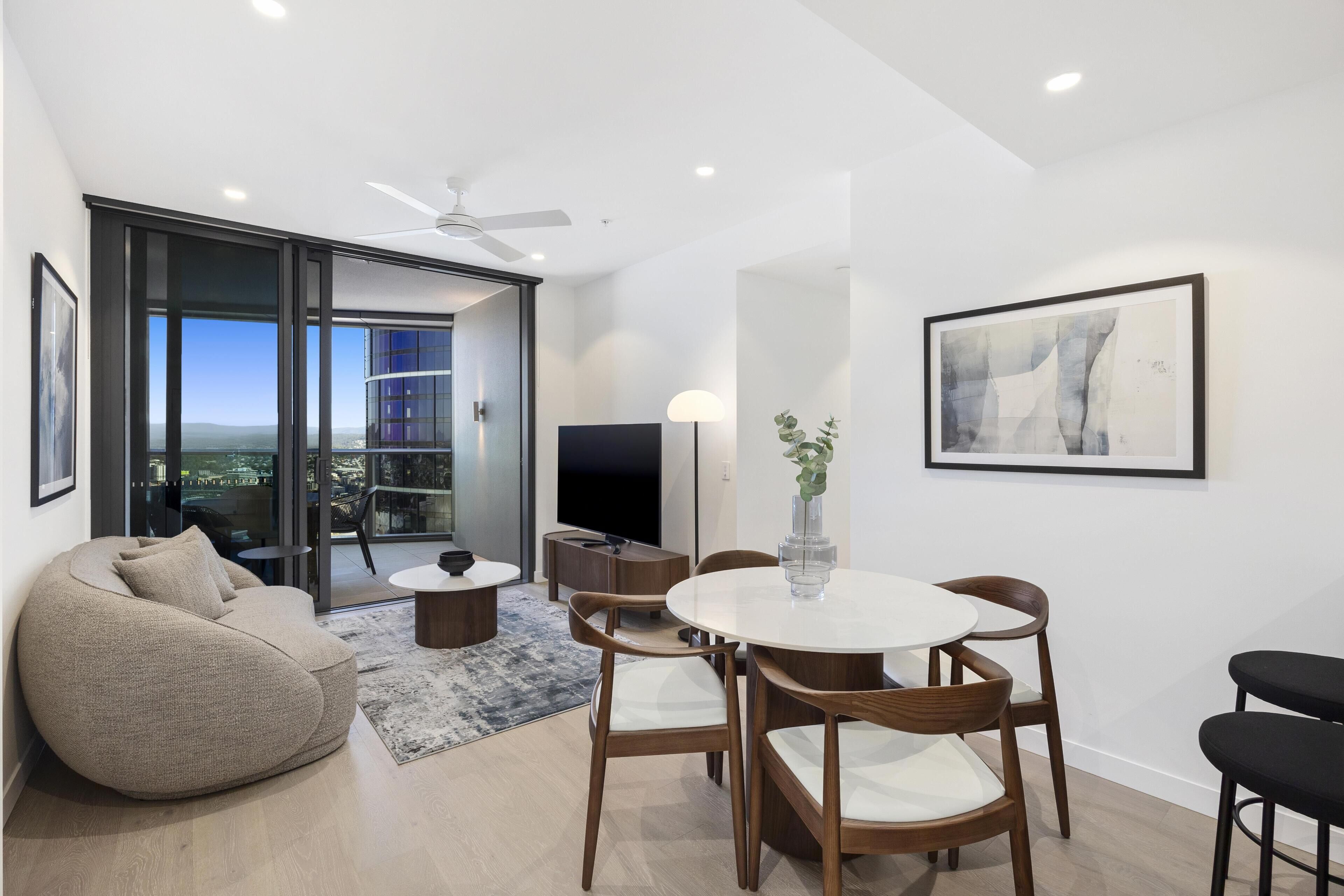 A modern living room with a large bean bag, a round dining table with chairs, a flat-screen TV, and a ceiling fan.