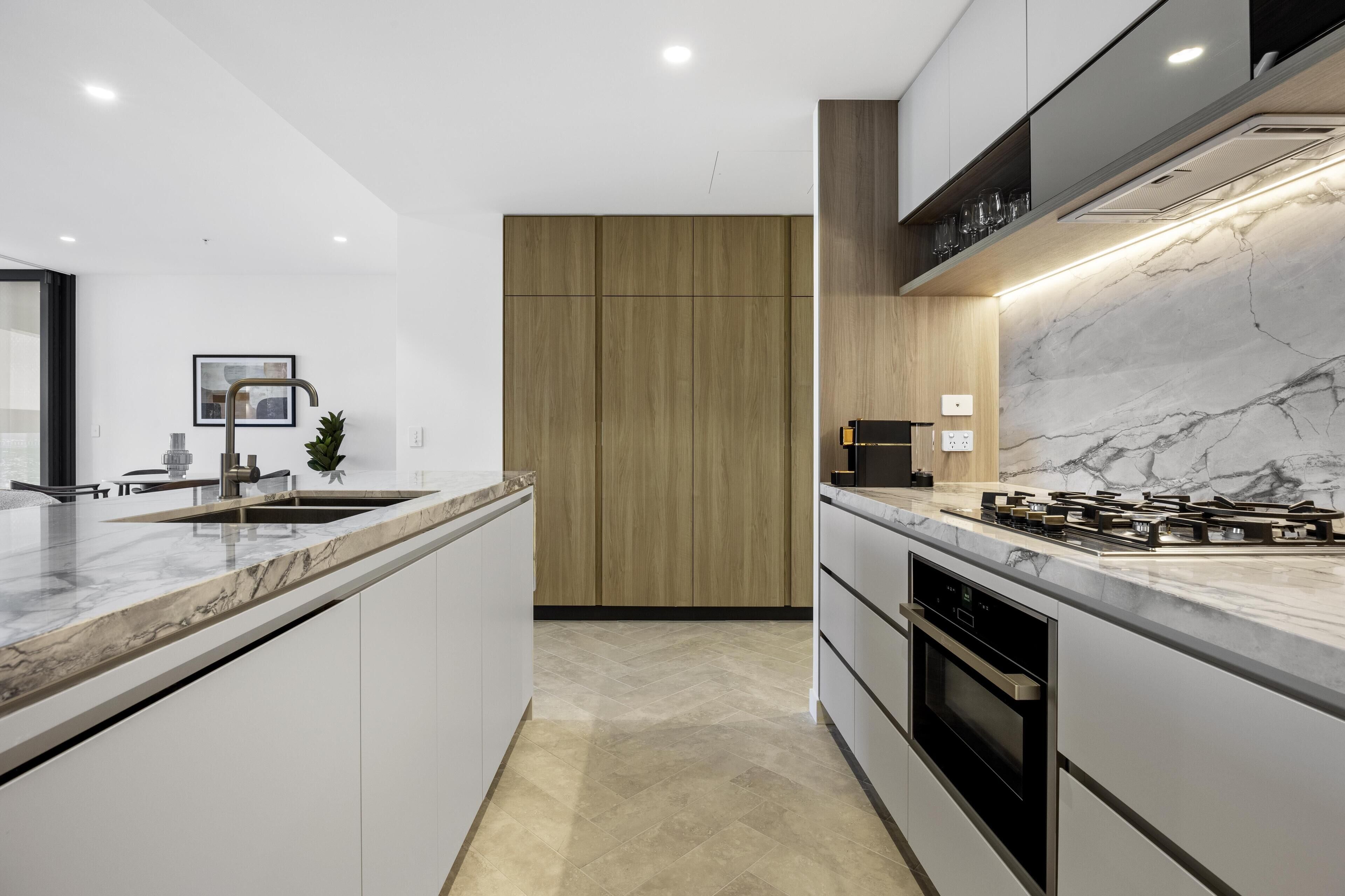 A modern kitchen with a marble countertop, built-in oven, and wooden cabinets.