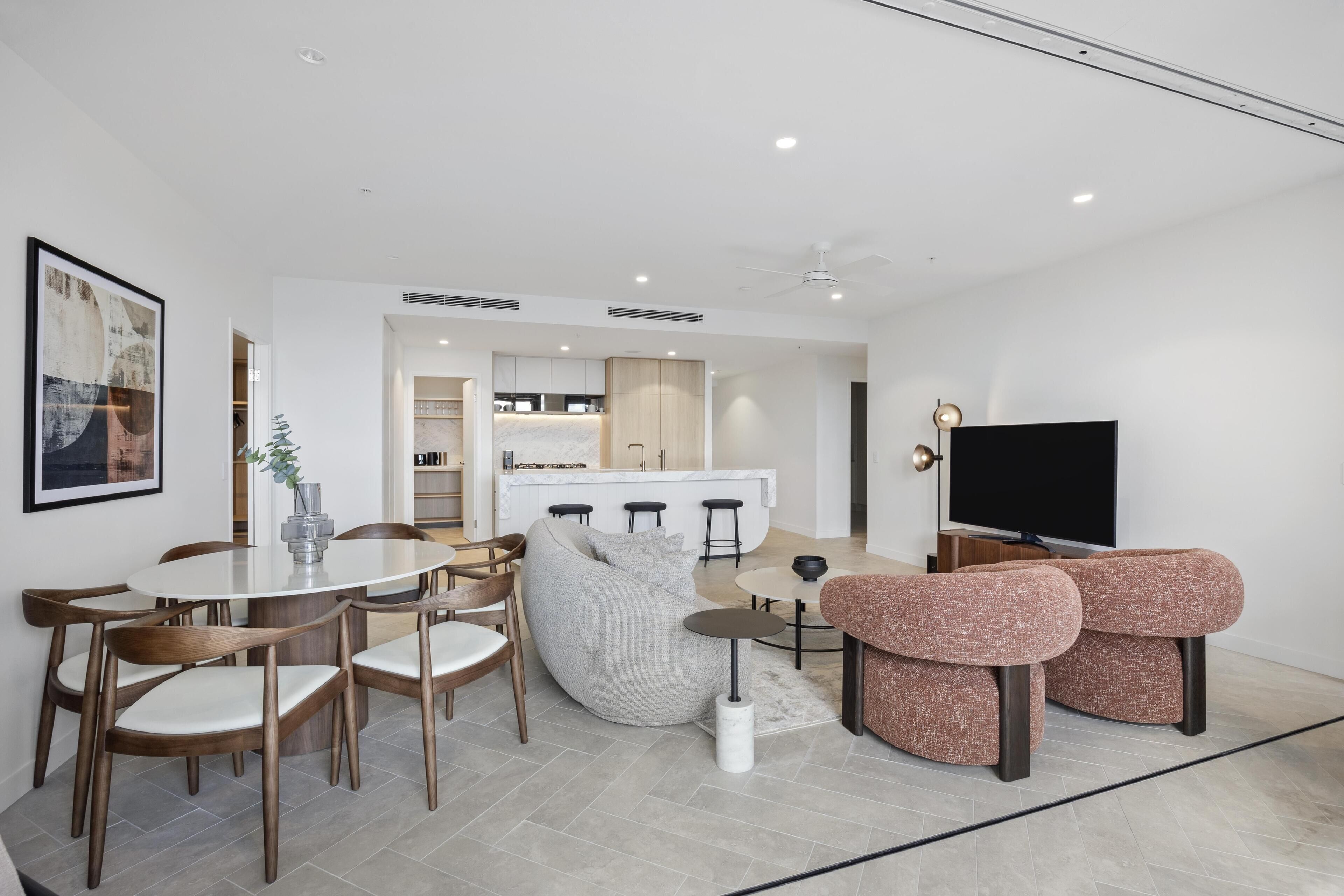 Un salon moderne avec un coin repas, une cuisine à l’arrière-plan et un téléviseur à écran plat.