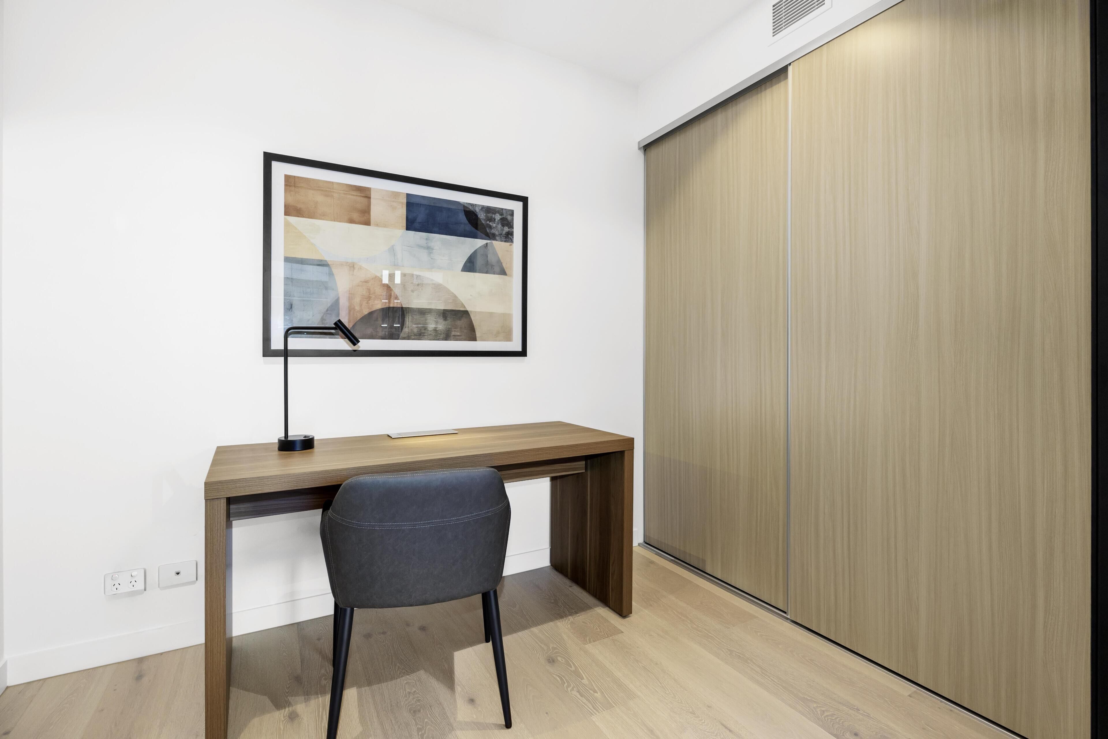 A modern office space with a wooden desk, a grey chair, and a framed abstract painting on the wall.