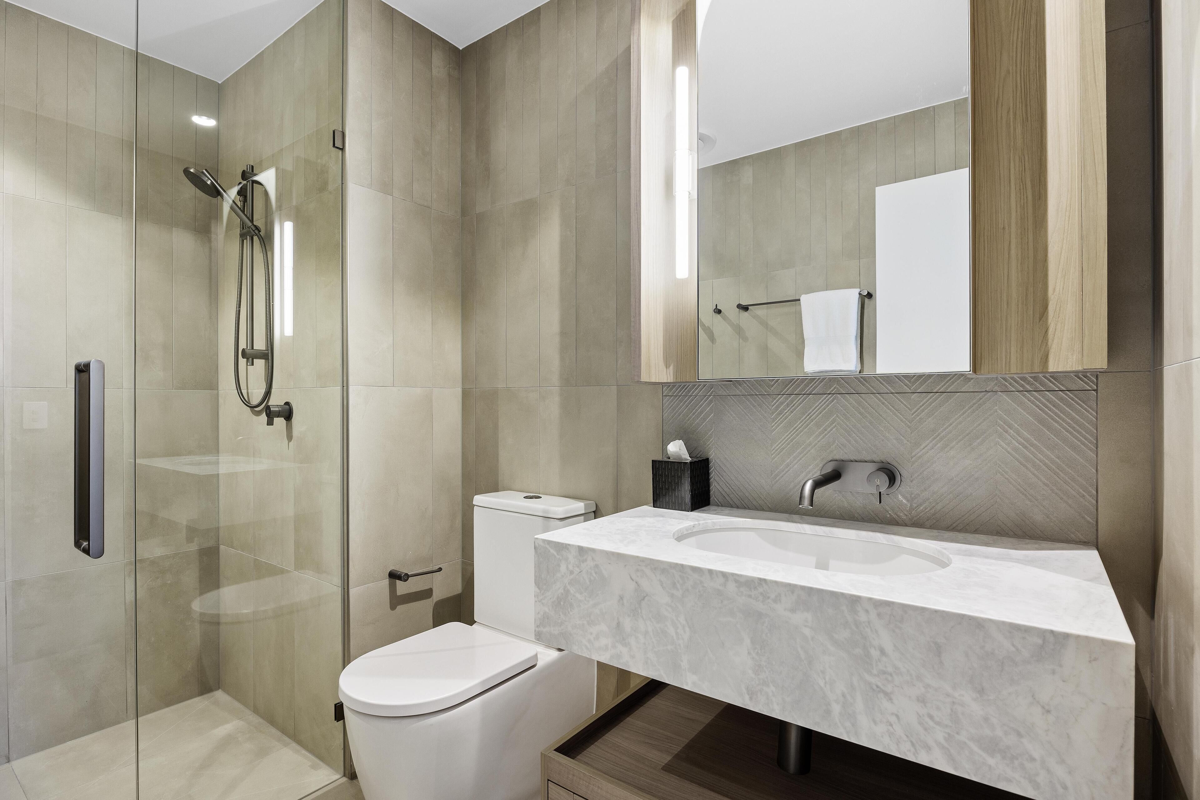 A modern bathroom with a glass-enclosed shower, a white toilet, and a marble sink with a large mirror above.