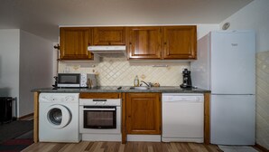 A compact kitchen with wooden cabinets, a microwave, a coffee maker, a washing machine, and a dishwasher. - Large, fully-equipped 8-pers apt (Allos)