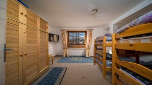 A compact room with bunk beds, a wooden wardrobe, a television, and a window with curtains. - Large, fully-equipped 8-pers apt (Allos)