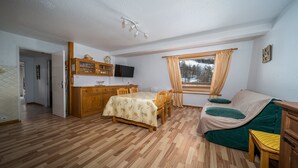 A cozy room with a wooden dining table, a sofa, a TV, and a window with curtains. - Large, fully-equipped 8-pers apt (Allos)