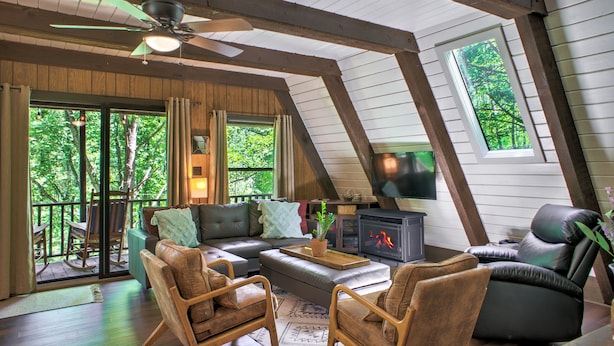 A cozy loft-style living room with a fireplace, comfortable seating, and large windows offering a view of the outdoors. - A-frame Cabin Near Mt. Mitchell | Rustic A-Frame on Private Acre (Burnsville)